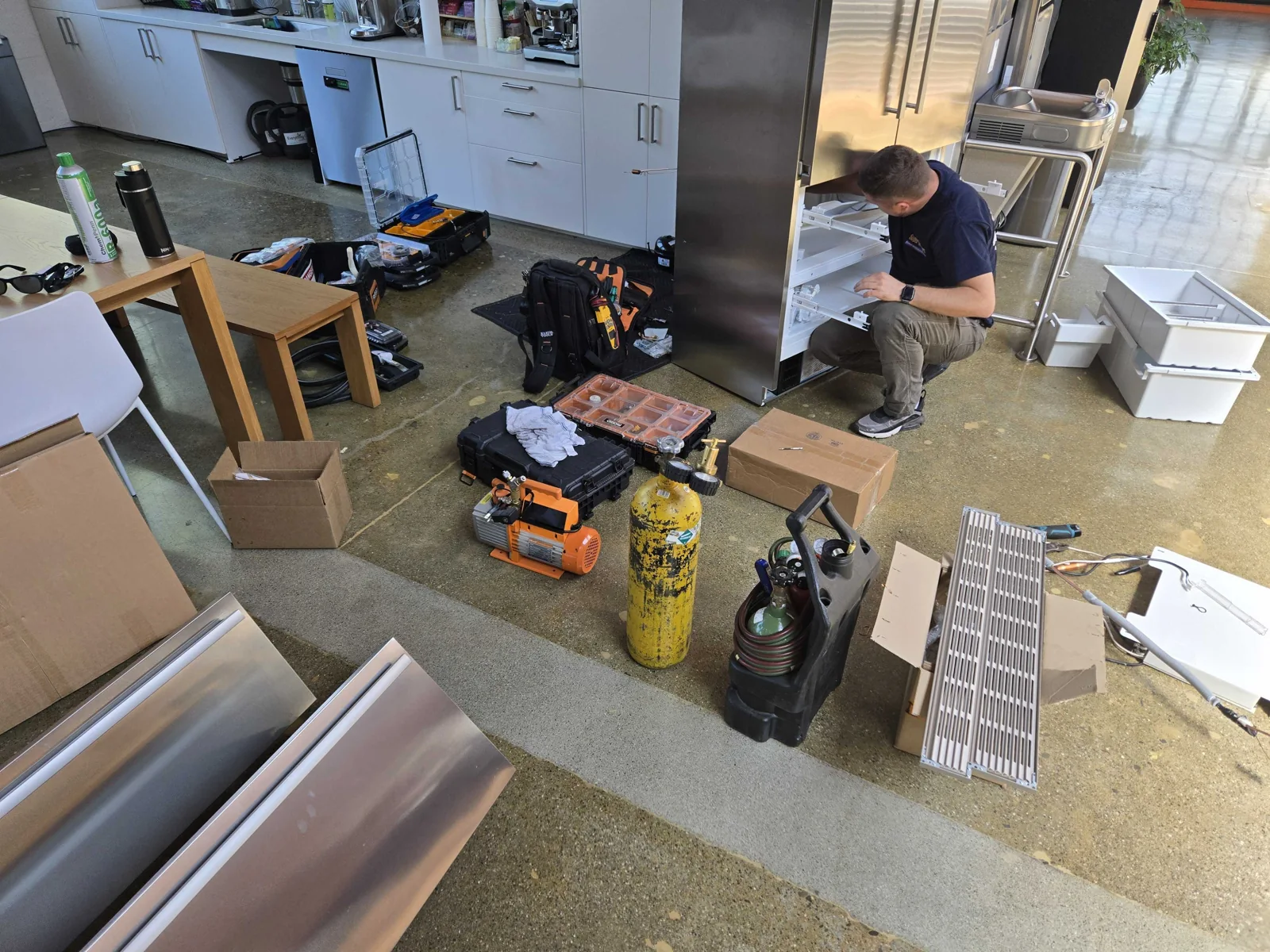 Technician working inside a refrigerator with drawers removed.