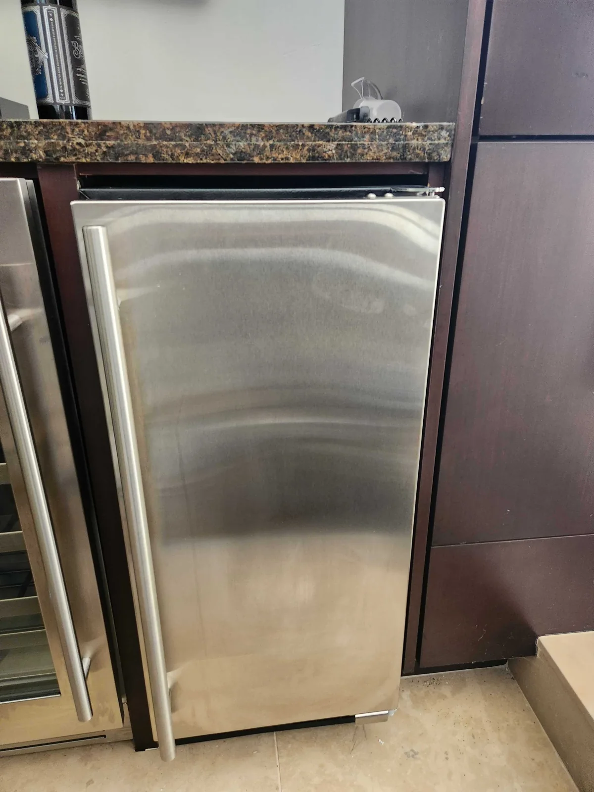 Stainless-steel undercounter ice maker installed beside cabinetry.