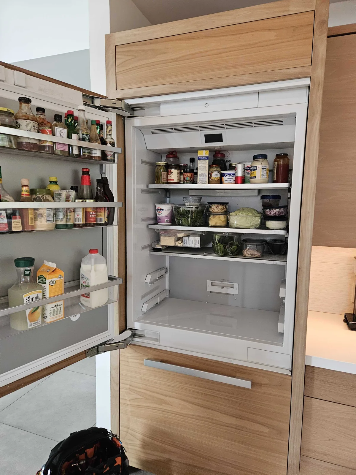 Open built-in Miele refrigerator with shelves and lower drawers visible.